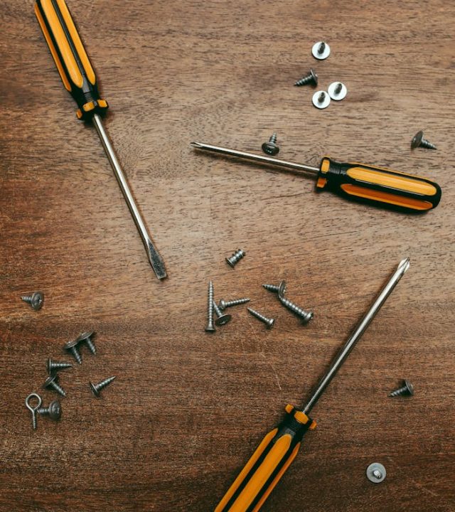 Flat lay of three screwdrivers and assorted screws on a wooden surface.
